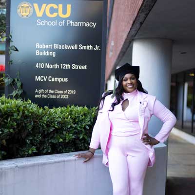 tayana cuffee in a graduation cap in front of the v.c.u. school of pharmacy building