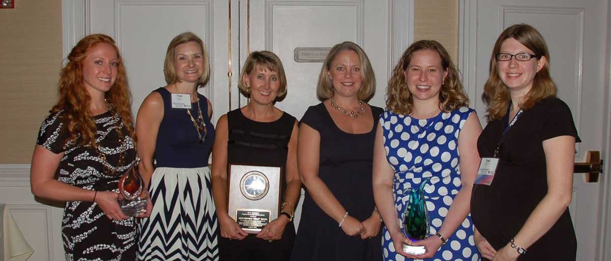 six smiling people at an awards reception with three holding awards